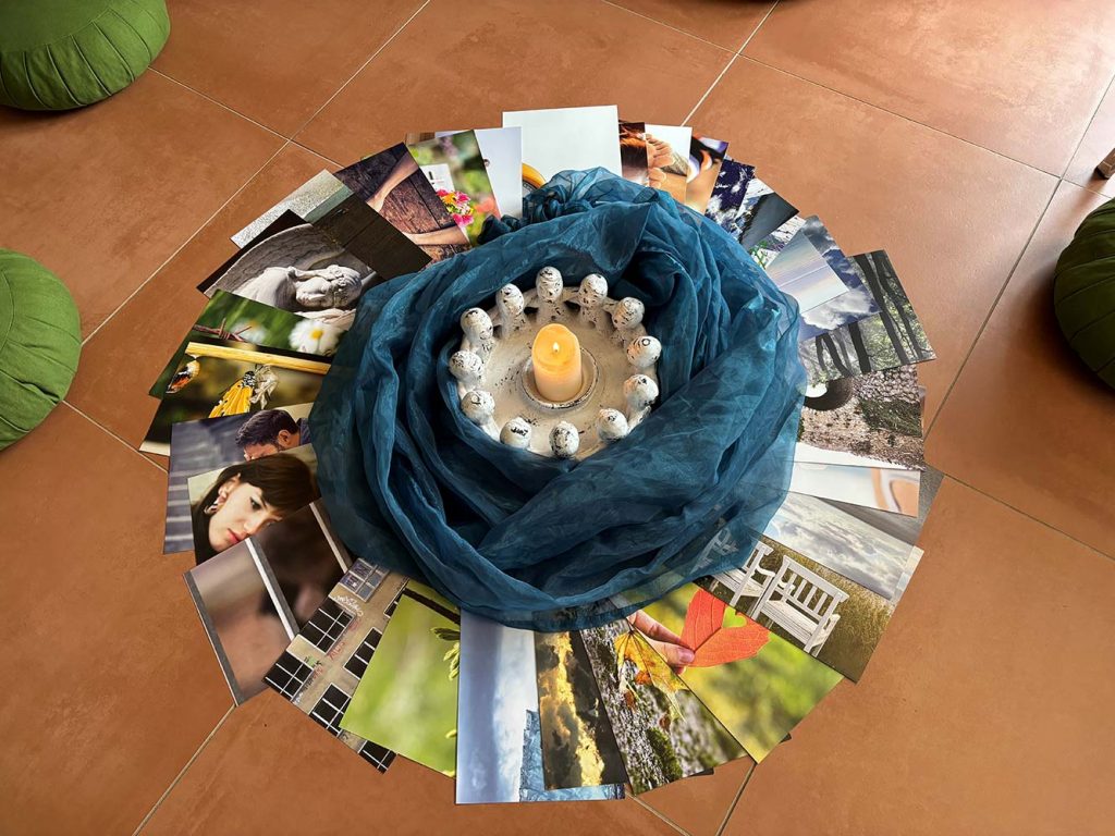 Kerze und kleine Figuren in einem blauen Tuch, umgeben von einem Kreis aus Fotos auf dem Boden